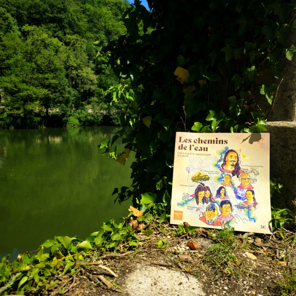 hoto du Journal N°2 posé sur un muret en pierre au bord de l'eau, avec une rivière paisible et une colline boisée en arrière-plan.